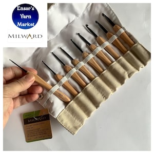 May include: A set of 9 wooden handled crochet hooks in a beige canvas roll. The hooks are arranged in order of size, with the smallest hook at the top and the largest hook at the bottom. The hooks are made of wood and have black metal hooks. The roll has a white label with the text "MILWARD Wooden Handle Crochet Hook Set" and a list of hook sizes.