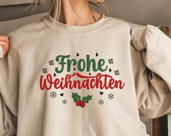 Può includere: Felpa beige con la scritta tedesca "Frohe Weihnachten" in verde e rosso. Il design include fiocchi di neve, agrifoglio e cuori. Un top a tema festivo.