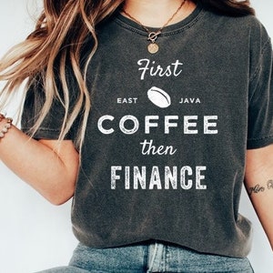 May include: A dark gray t-shirt with the text "First East Java Coffee then Finance" in white lettering. The text is stylized with a coffee bean graphic.