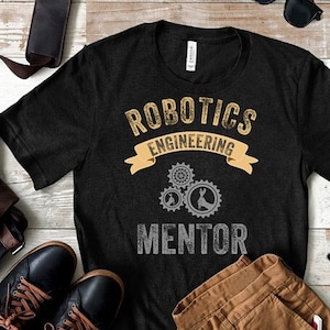 Peut inclure: T-shirt noir avec le texte "Robotics Engineering Mentor" en blanc avec un ruban jaune et des engrenages gris.
