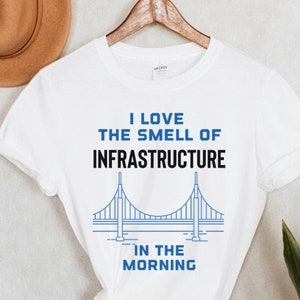 May include: White t-shirt with a blue and black graphic of a bridge and the text "I love the smell of infrastructure in the morning".
