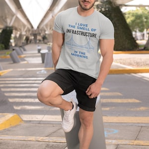 May include: A light gray t-shirt with a blue bridge graphic and the text "I love the smell of infrastructure in the morning".