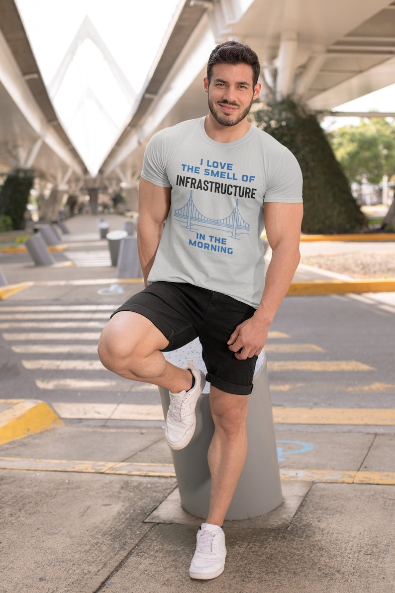 May include: A light gray t-shirt with a blue bridge graphic and the text "I love the smell of infrastructure in the morning".