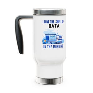 May include: A white ceramic mug with a black handle and the text "But First, Coffee" in a bold, black font. The mug is set against a blurred background, highlighting its clean design.