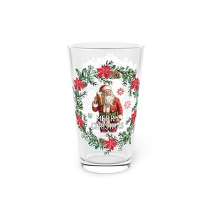 May include: A clear pint glass with a Christmas-themed design. The glass features a watercolor illustration of Santa Claus holding a beer, surrounded by a wreath of red poinsettias, pine cones, and greenery. The words "MERRY CHRISTMAS" are printed below Santa.