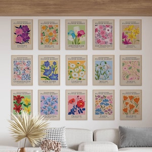 Puede incluir: Un conjunto de 15 impresiones digitales con ilustraciones de mercado de flores de estilo vintage. Cada impresi&oacute;n presenta el nombre de una ciudad diferente y un dise&ntilde;o floral &uacute;nico. Las impresiones se muestran en una pared blanca en un sal&oacute;n.