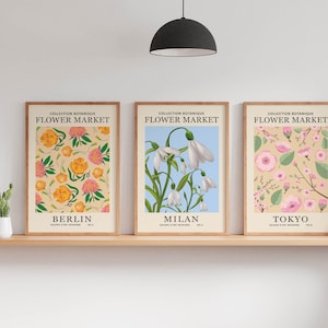 Puede incluir: Tres impresiones bot&aacute;nicas enmarcadas con el t&iacute;tulo "Flower Market" y las ciudades "Berl&iacute;n", "Mil&aacute;n" y "Tokio" debajo. Las impresiones presentan diferentes patrones florales en tonos de rosa, amarillo, blanco y verde.
