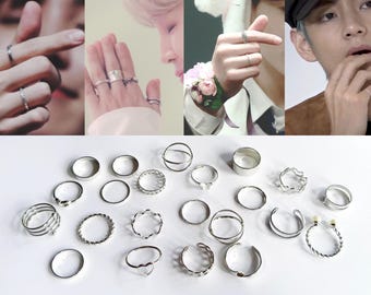 May include: A collection of twenty-two silver-toned metal rings in various designs, including plain bands, twisted textures, open-ended styles, and heart-shaped accents, displayed alongside four separate images of rings worn on fingers.