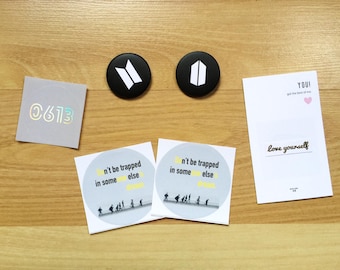 Può includere: Due pulsanti rotondi in bianco e nero con un logo stilizzato. Due adesivi bianchi con il testo "Non rimanere intrappolato in qualcos'altro" e un gruppo di persone che camminano. Una carta bianca con il testo "YOU! Get the best of me" e "Love yourself".