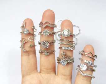 May include: A hand model wearing a variety of silver rings with clear cubic zirconia stones. The rings are stacked on each finger and feature different designs, including a crescent moon, a star, a triangle, and a wavy line.