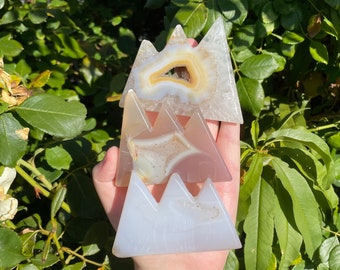 May include: Three agate crystal mountains in shades of white, pink, and brown. The top mountain has a natural hole in the centre.