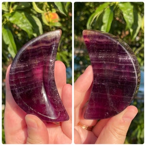 Peut inclure: Un cristal de lune en fluorite de couleur violette et verte. Le cristal est poli et a une surface lisse et brillante.