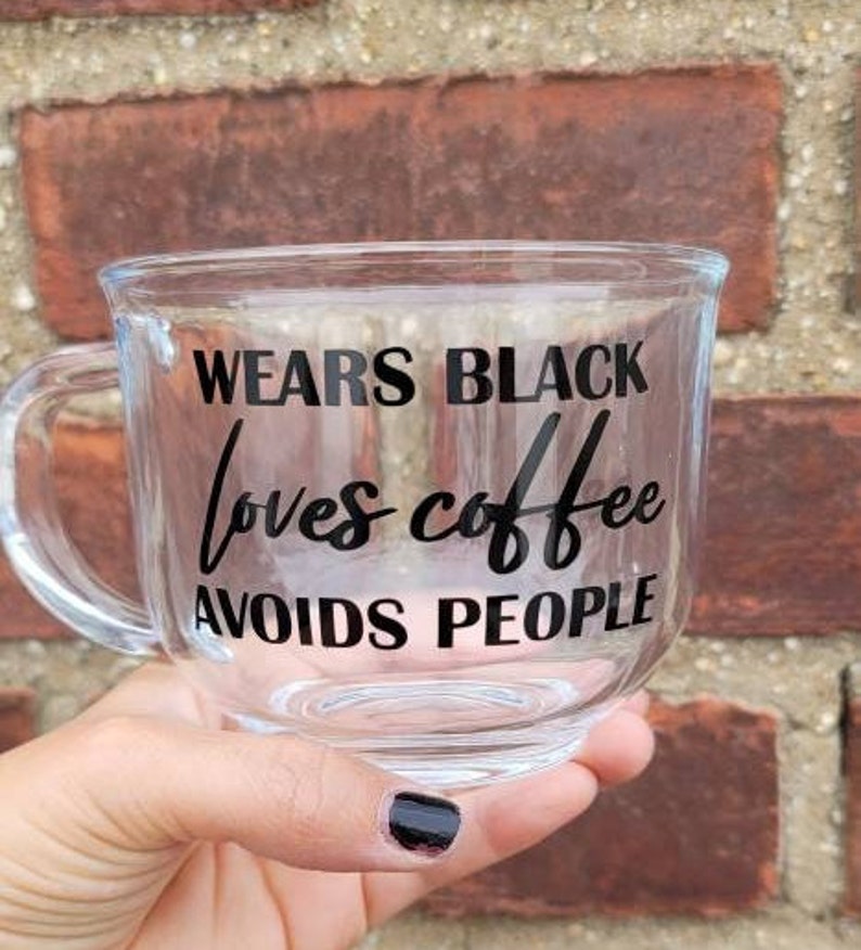 May include: A clear glass mug with a black inscription that reads "Wears Black Loves Coffee Avoids People".