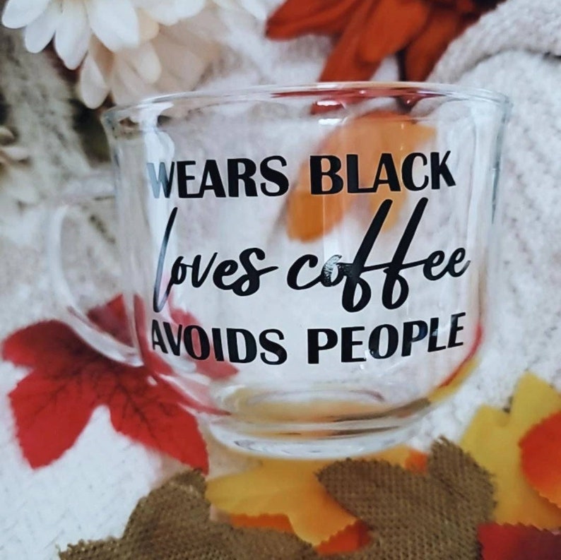 May include: A clear glass mug with a black inscription that reads "Wears Black Loves Coffee Avoids People".