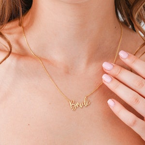 May include: A gold necklace with a cursive 'Bride' pendant.