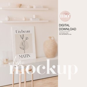 May include: A white frame mockup with a beige background and a black line drawing of a flower with the text "Un beau matin" in black. The frame is sitting on a white shelf with a beige vase and other decorative items.