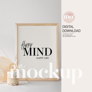 Könnte beinhalten: Ein Mockup eines gerahmten Drucks mit dem Text "Happy MIND HAPPY LIFE" in schwarzen Buchstaben auf weißem Hintergrund. Der Rahmen ist aus hellem Holz und steht auf einer weißen Oberfläche.