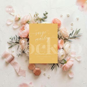 May include: A mustard yellow wedding invitation with white script, surrounded by pink and white flowers, greenery, and a pink ribbon. The invitation reads "Saige & Marley" and includes event details.