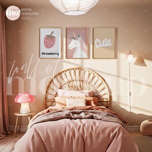 Puede incluir: Una escena de dormitorio con una cama con edredón rosa y cabecero tejido. Encima de la cama hay tres obras de arte enmarcadas: una fresa, un unicornio y la palabra "Cute". Una lámpara con forma de hongo está sobre una mesita.