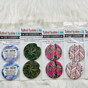 May include: A collection of car coasters with various designs, including baseballs, cannabis leaves, pink and brown chevron patterns, and a Starbucks/Target logo mashup. Each coaster is packaged and labeled with the text "Redhead Kreations & More".