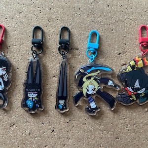 Puede incluir: Cinco llaveros coloridos con personajes de estilo anime. Cada llavero tiene un personaje en blanco y negro con un diseño y una combinación de colores únicos. Los llaveros están hechos de acrílico transparente y tienen un anillo de metal para sujetarlos a las llaves.