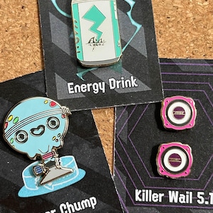May include: Three enamel pins featuring a blue and green energy drink can with the text "A.E.L.X. ACTIVE", a blue and green cartoon character with the text "Super Chump", and two pink and gold speaker pins with the text "Killer Wail 57."