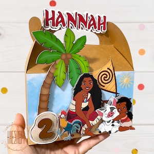 May include: A brown cardboard favor box with a Moana theme. The box features a palm tree, Moana, Pua the pig, and a rooster. The box is decorated with a blue and white background and has the name "HANNAH" and the number "2" on it.