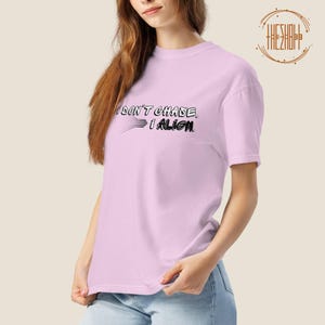 Pode incluir: T-shirt rosa claro com o texto preto "I DON'T CHASE. I ALIGN". O design inclui linhas que se estendem da palavra "CHASE". A t-shirt tem mangas curtas e gola redonda.