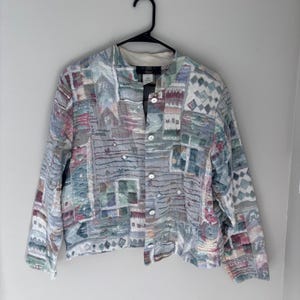May include: A long-sleeve button-up jacket featuring a multi-colored patchwork design with shades of blue, pink, green, and white. The garment has a mandarin collar, a front button closure, and a textured fabric surface with various geometric patterns.