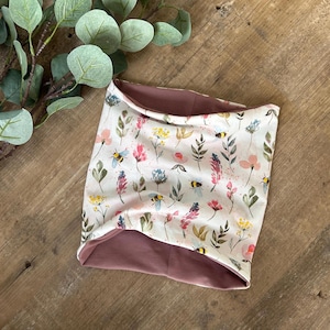 Könnte beinhalten: Ein wendbarer Halsschmeichler mit einem Blumenmuster mit Bienen und Blättern auf der einen Seite und einer einfarbigen, staubigen Rosenfarbe auf der anderen Seite.