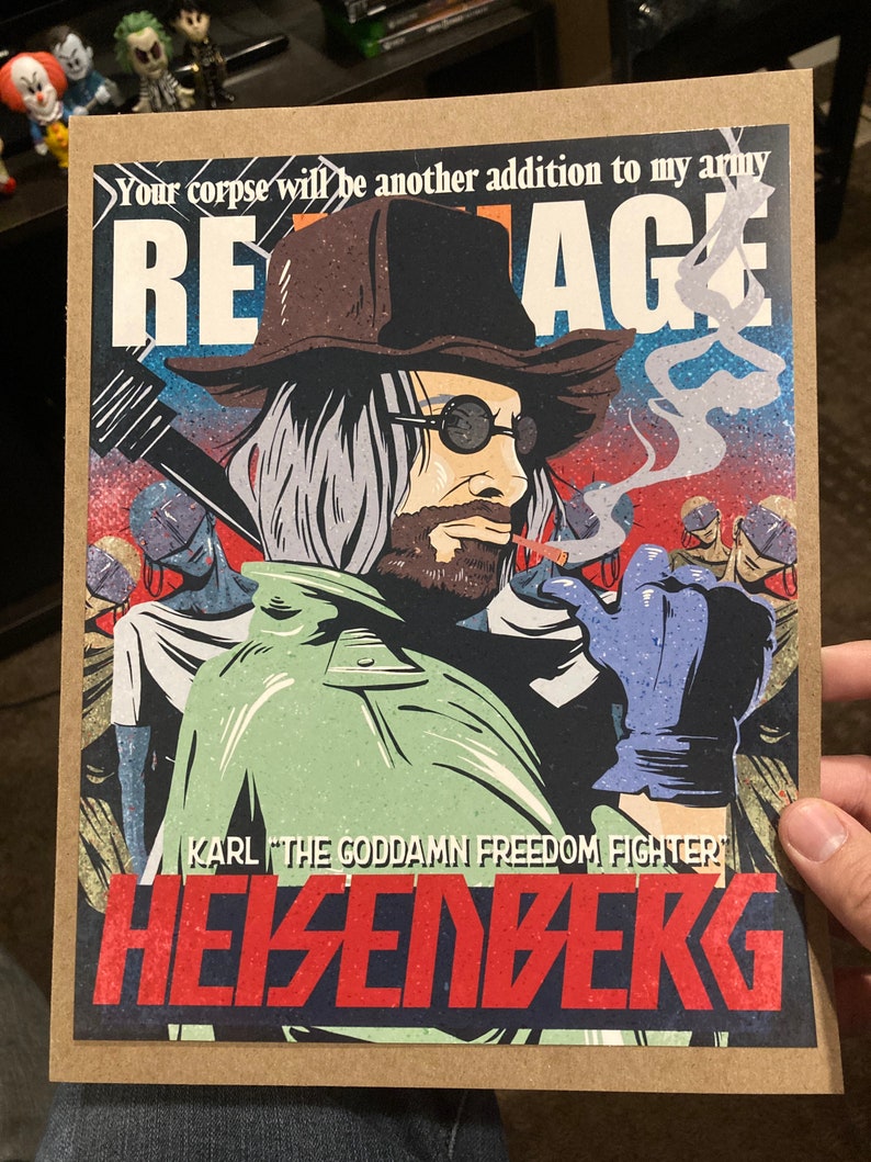 May include: A graphic art print featuring a character with a hat, sunglasses, and a beard, smoking a cigarette. The print includes the text "REAGE", "KARL THE GODDAMN FREEDOM FIGHTER", and "HEISENBERG". The artwork has a vintage comic book style.