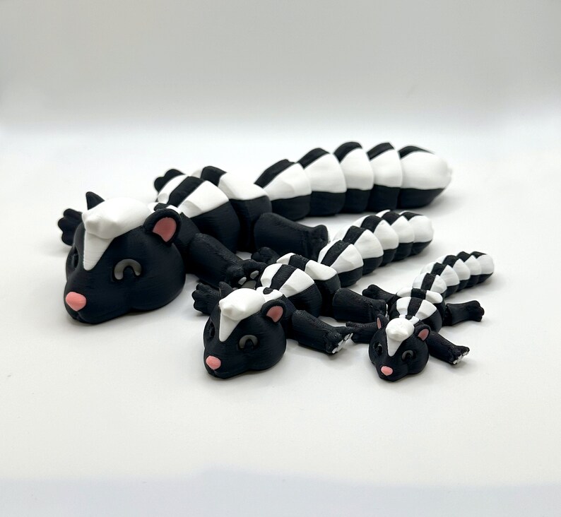 May include: Three black and white skunk figurines of varying sizes. The largest skunk is lying on its belly with its tail curled up. The medium-sized skunk is lying on its belly with its tail straight out. The smallest skunk is lying on its belly with its tail curled up.