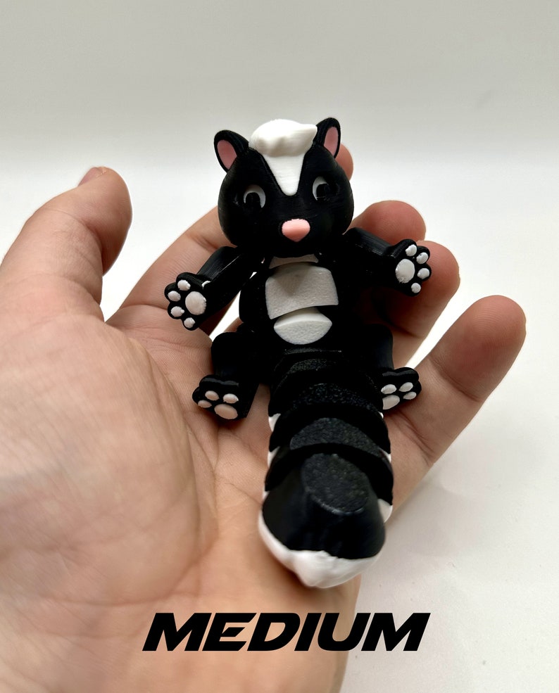 May include: Black and white skunk-shaped fidget toy with a segmented tail. The toy is in the "medium" size.