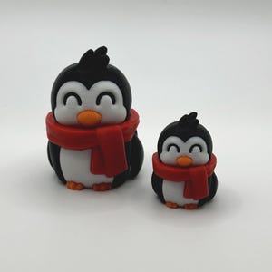 Op de afbeelding: Twee pingu&iuml;nbeeldjes. De pingu&iuml;ns zijn zwart en wit met oranje snavels en voeten. Elke pingu&iuml;n draagt een rode sjaal. De grotere pingu&iuml;n is ongeveer 7.6 cm hoog en de kleinere ongeveer 5 cm hoog.