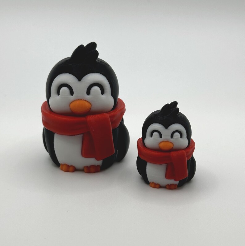 Op de afbeelding: Twee pingu&iuml;nbeeldjes. De pingu&iuml;ns zijn zwart en wit met oranje snavels en voeten. Elke pingu&iuml;n draagt een rode sjaal. De grotere pingu&iuml;n is ongeveer 7.6 cm hoog en de kleinere ongeveer 5 cm hoog.