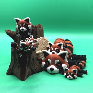 May include: A collection of red panda figurines in various poses. Some are perched on a brown tree stump, while others are lying down. The pandas have white and black markings on their faces and bodies, with a green background.