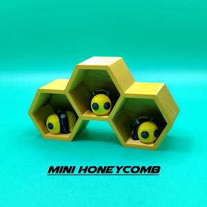 May include: A yellow honeycomb-shaped shelf with three compartments, each containing a small yellow and black bee figurine. The shelf is labeled "MINI HONEYCOMB".