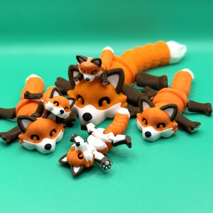 May include: Five orange and brown articulated fox figurines, some with white accents, are posed in a playful manner on a green background.