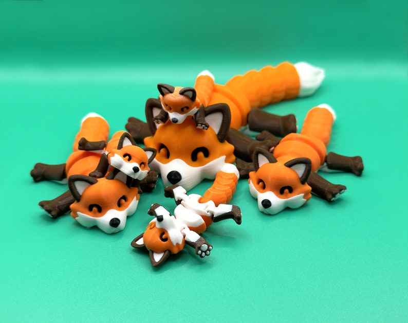 May include: Five orange and brown articulated fox figurines, some with white accents, are posed in a playful manner on a green background.
