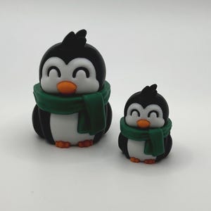 Op de afbeelding: Twee pingu&iuml;nbeeldjes. De pingu&iuml;ns zijn zwart en wit met oranje snavels en voeten. Elke pingu&iuml;n draagt een groene sjaal. De ene pingu&iuml;n is groter dan de andere.