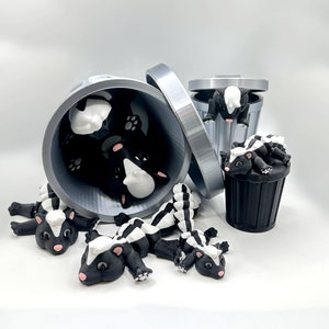 May include: A set of black and white skunk figurines in various poses, some inside a silver trash can, others on a white surface.