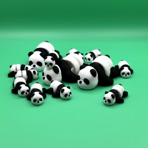 Puede incluir: Un grupo de 11 peque&ntilde;as figuras de panda blancas y negras. Los pandas est&aacute;n en varias poses, algunos est&aacute;n acostados, otros est&aacute;n sentados y otros est&aacute;n de pie. Los pandas est&aacute;n hechos de un pl&aacute;stico blanco liso con detalles pintados en negro.