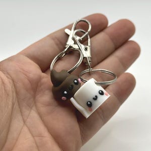 Pu&ograve; includere: Un portachiavi originale con due piccoli ciondoli in stile cartone animato. Uno &egrave; un'emoji di cacca marrone sorridente, e l'altro &egrave; un rotolo di carta igienica bianca sorridente. Entrambi i ciondoli hanno occhi neri e guance rosa, attaccati a un portachiavi argentato.