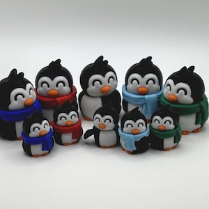 Op de afbeelding: Een verzameling zwart-witte pingu&iuml;nbeeldjes met oranje snavels en voeten. Elke pingu&iuml;n draagt een sjaal in verschillende kleuren, waaronder rood, blauw en groen. De pingu&iuml;ns vari&euml;ren in grootte, waardoor een familieachtige opstelling ontstaat.