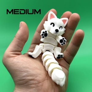 May include: White articulated toy fox with black paw prints. The toy is posed sitting with its tail curled up. The toy is about 5 inches tall.