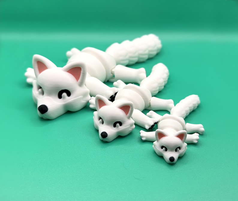 May include: Three white articulated fox figurines in different sizes. The largest fox is lying down with its head turned to the side. The medium-sized fox is lying down with its head turned to the side. The smallest fox is lying down with its head turned to the side.