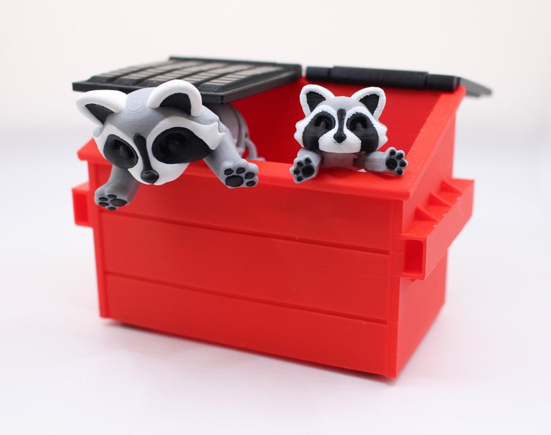 May include: Two raccoons peeking out of a red plastic trash can with a black lid. The raccoons are white and gray with black eyes and noses.