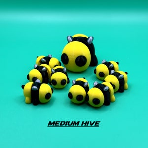 May include: A group of nine yellow and black bee figurines, with black eyes and silver accents. The figurines are arranged in a circle, with the largest bee in the center. The text "MEDIUM HIVE" is printed below the figurines.