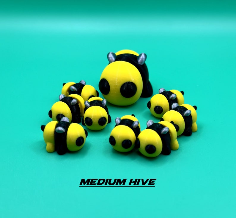 May include: A group of nine yellow and black bee figurines, with black eyes and silver accents. The figurines are arranged in a circle, with the largest bee in the center. The text "MEDIUM HIVE" is printed below the figurines.
