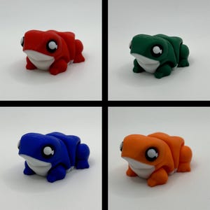 May include: Four colourful frog figurines in red, green, blue, and orange. Each frog has a white belly and large, round eyes. The frogs are in a playful, cartoon style, suitable for a child's room or as a whimsical desk accessory.